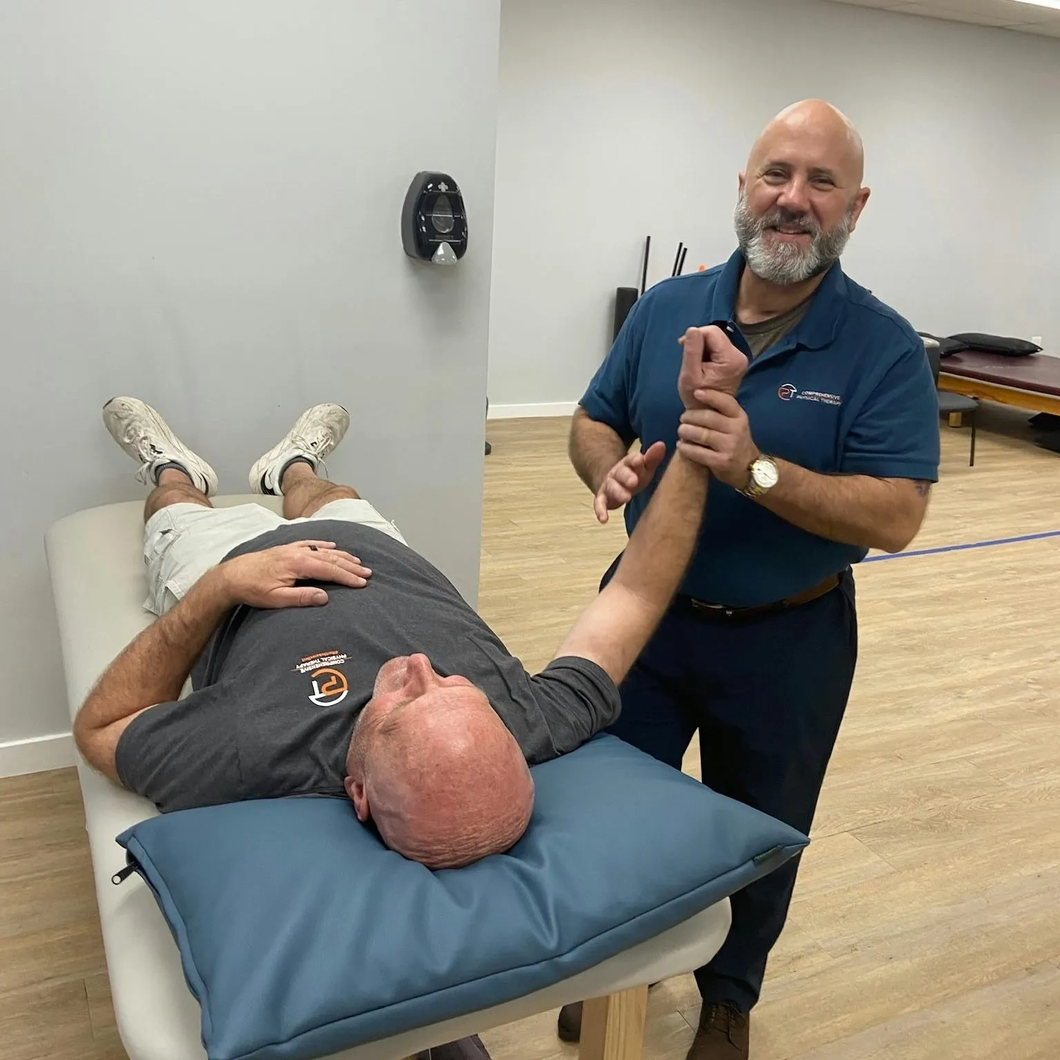Physical therapist performing manual arm and shoulder therapy on a patient lying on a treatment table