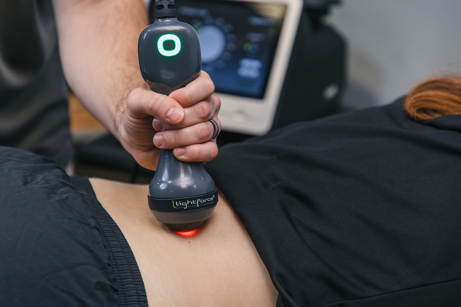 A clinician holding a therapy laser over a patient’s shoulder during treatment