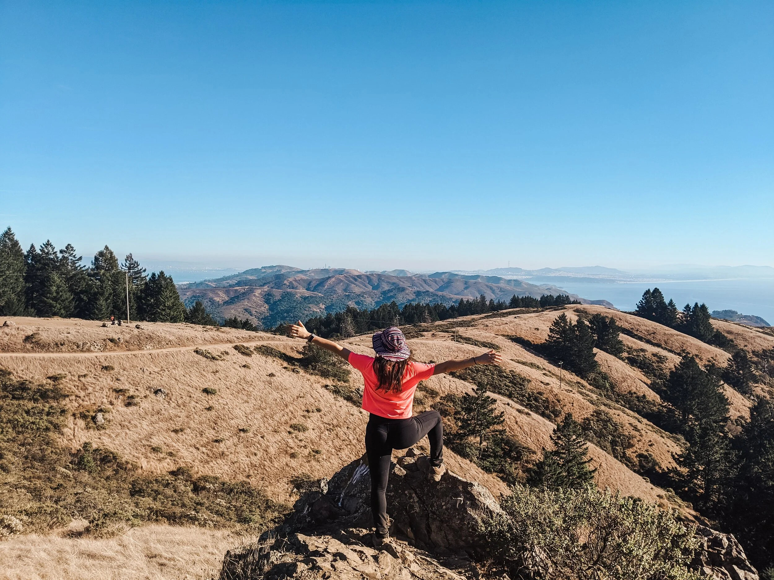 A hiker with arms outstretched on a rocky ridge above a valley