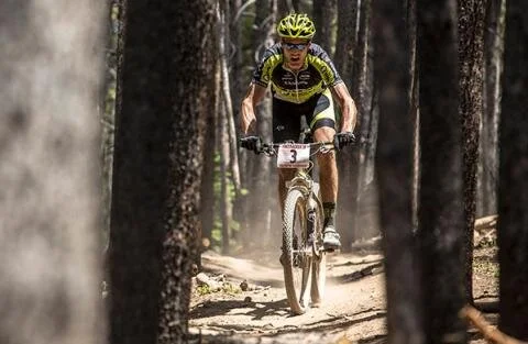 A mountain bike racer riding a dirt trail through a forest