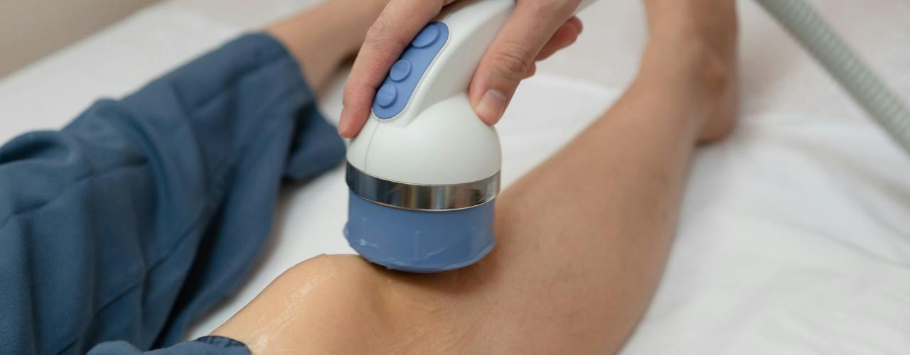 A handheld shockwave applicator on a patient's knee