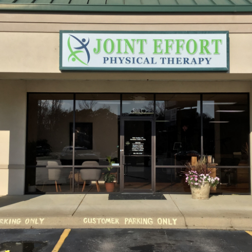The front of the clinic: glass doors under the Joint Effort Physical Therapy sign, with a planter of flowers outside