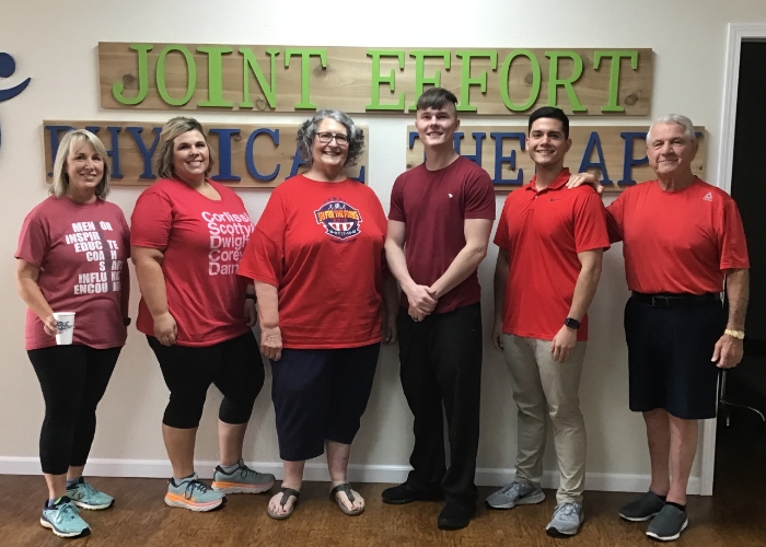 Six people in red shirts standing under the Joint Effort Physical Therapy sign