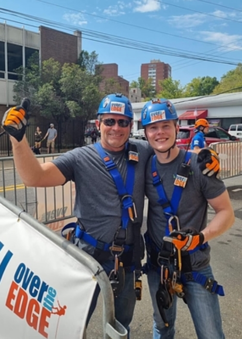Two team members in climbing helmets and harnesses at an Over the Edge charity event