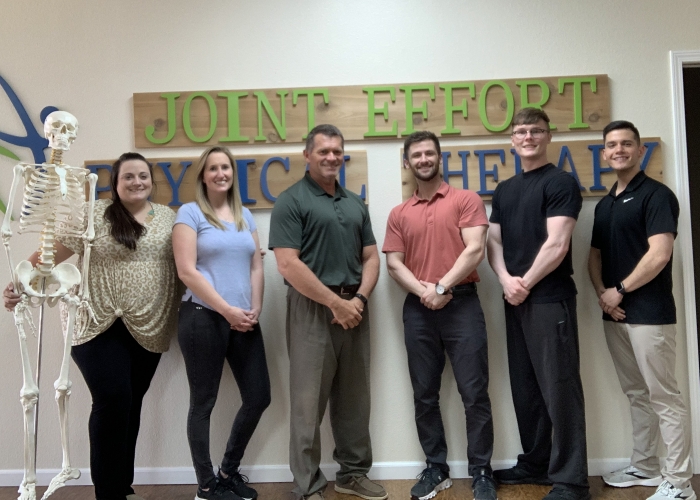 Six team members standing under the Joint Effort Physical Therapy sign