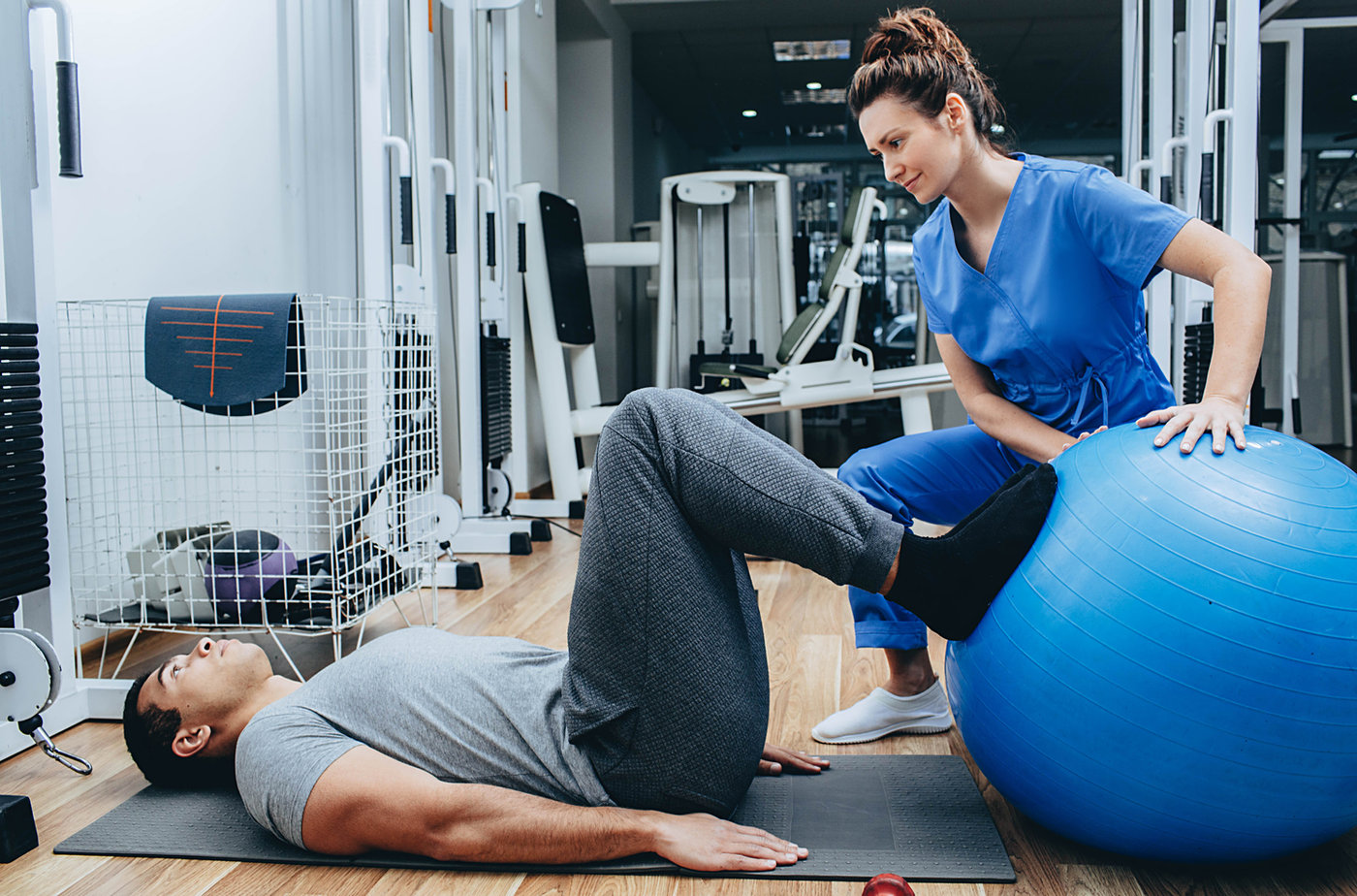 A physical therapist guiding a patient through a hip and core strengthening exercise on a physio ball