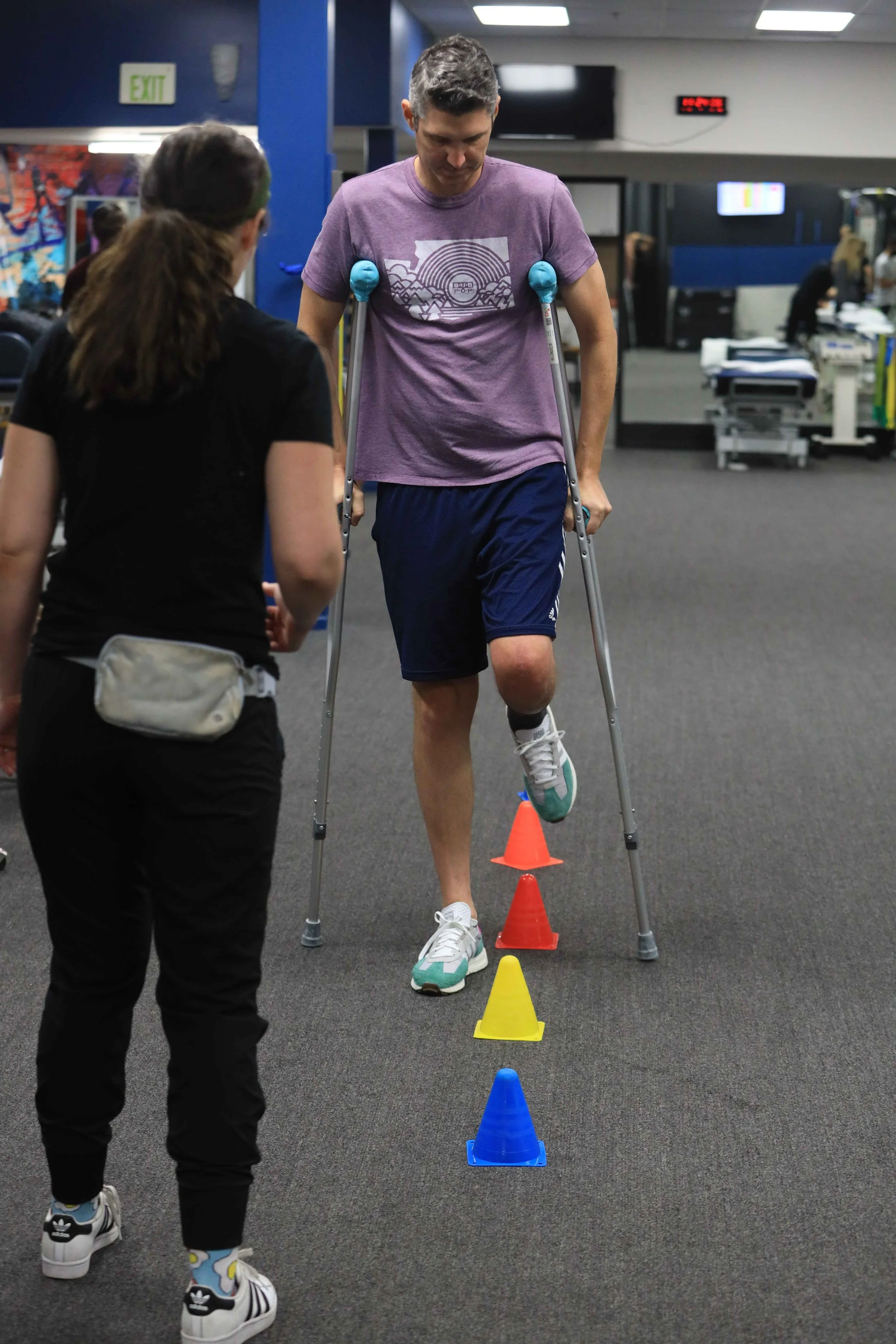 A man on crutches stepping over cones while a clinician guides him in the LOR gym
