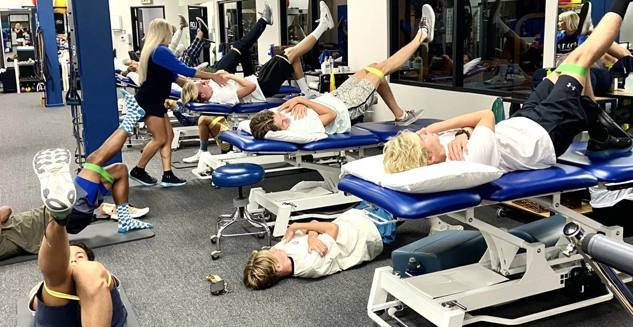 People lying on treatment tables lifting their legs with resistance bands in a group session at the LOR clinic