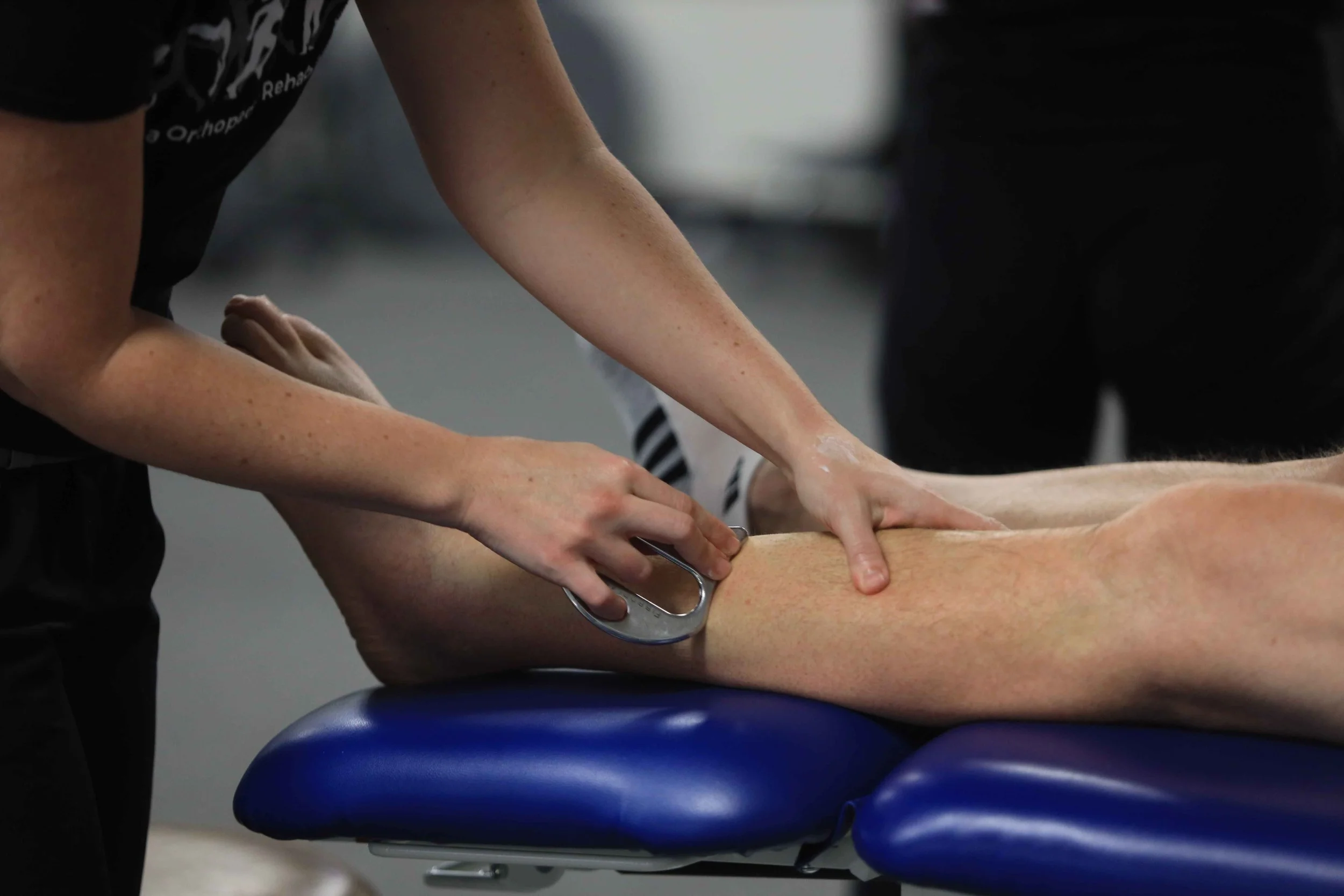 A LOR clinician treating a patient’s calf with her hands and a handheld tool while the patient lies on a treatment table