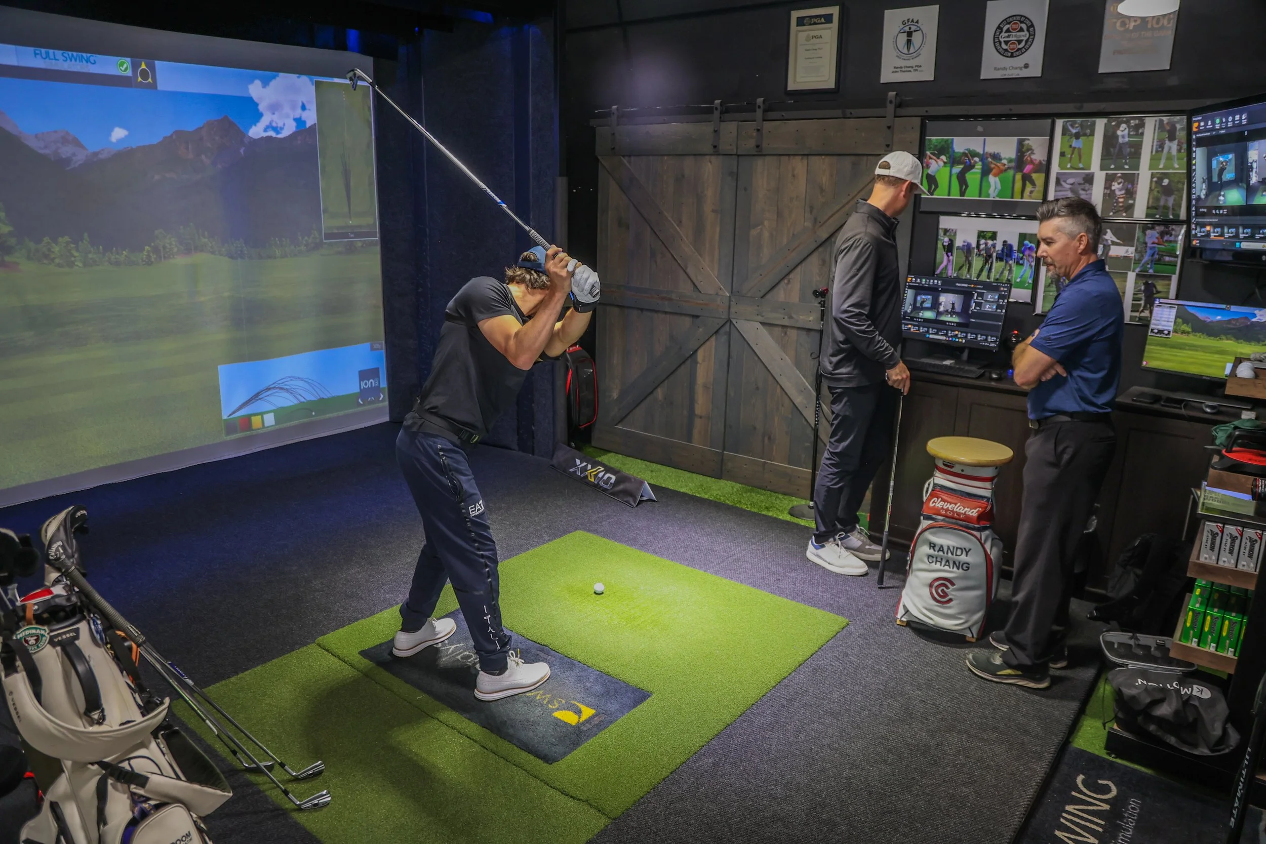 A golfer takes a swing on the Sports Lab mat in front of a motion capture screen while two people watch