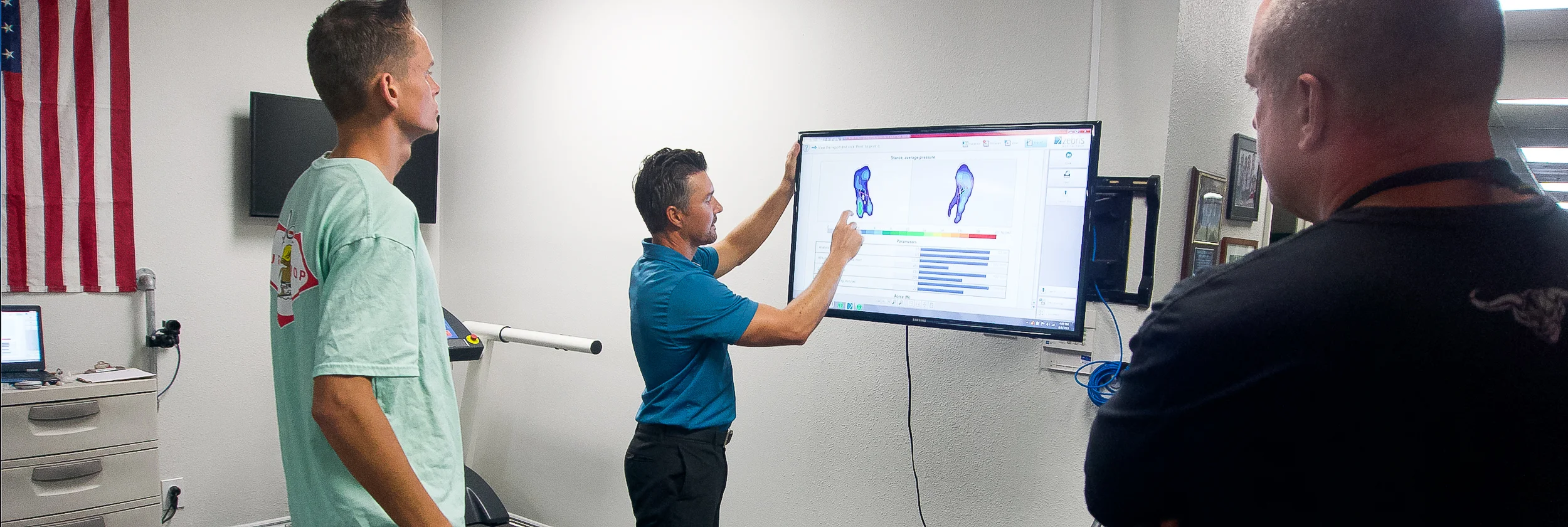A LOR clinician pointing to foot pressure data on a screen while two people watch