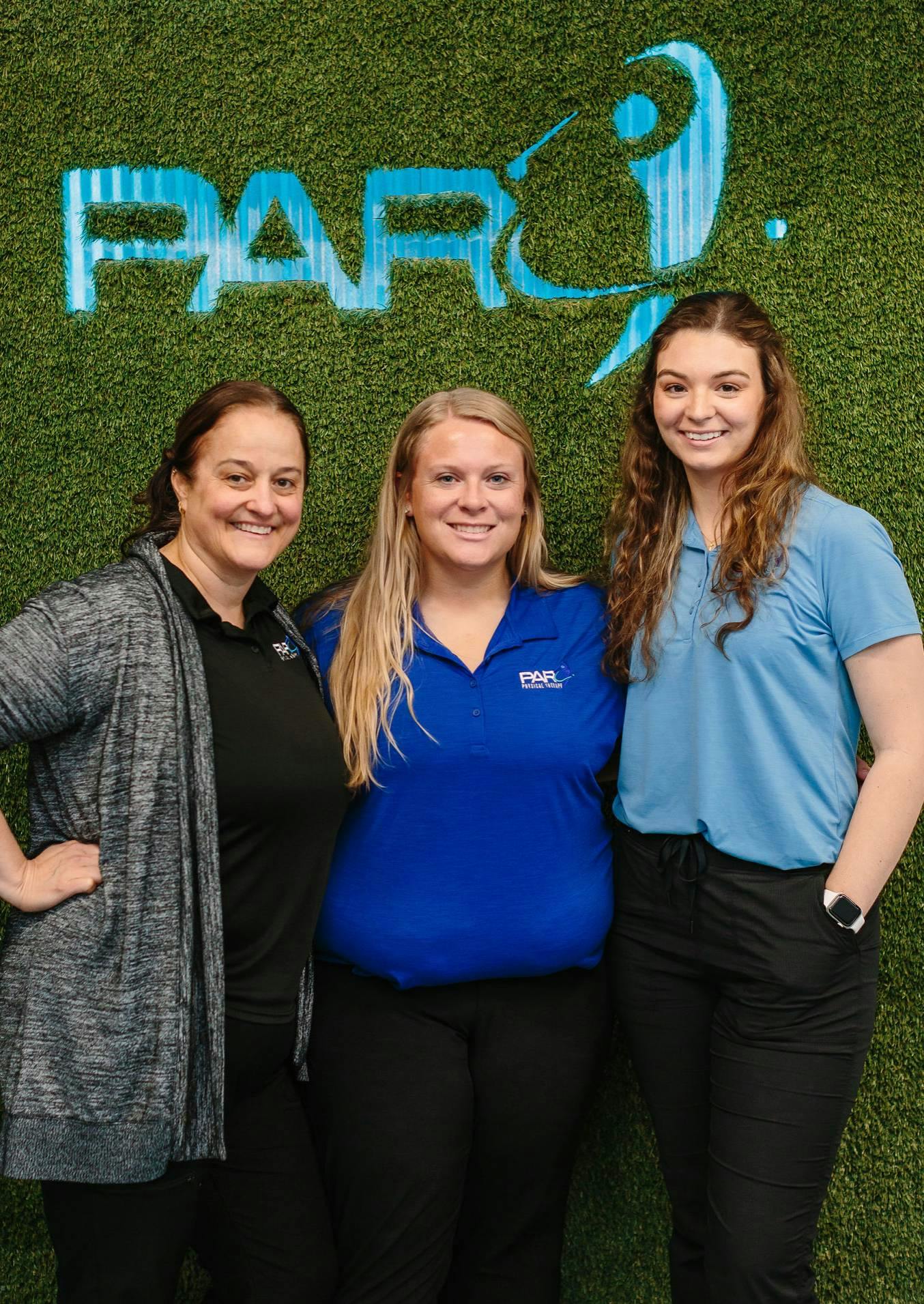 Three members of the PAR team standing in front of the PAR logo on a green wall