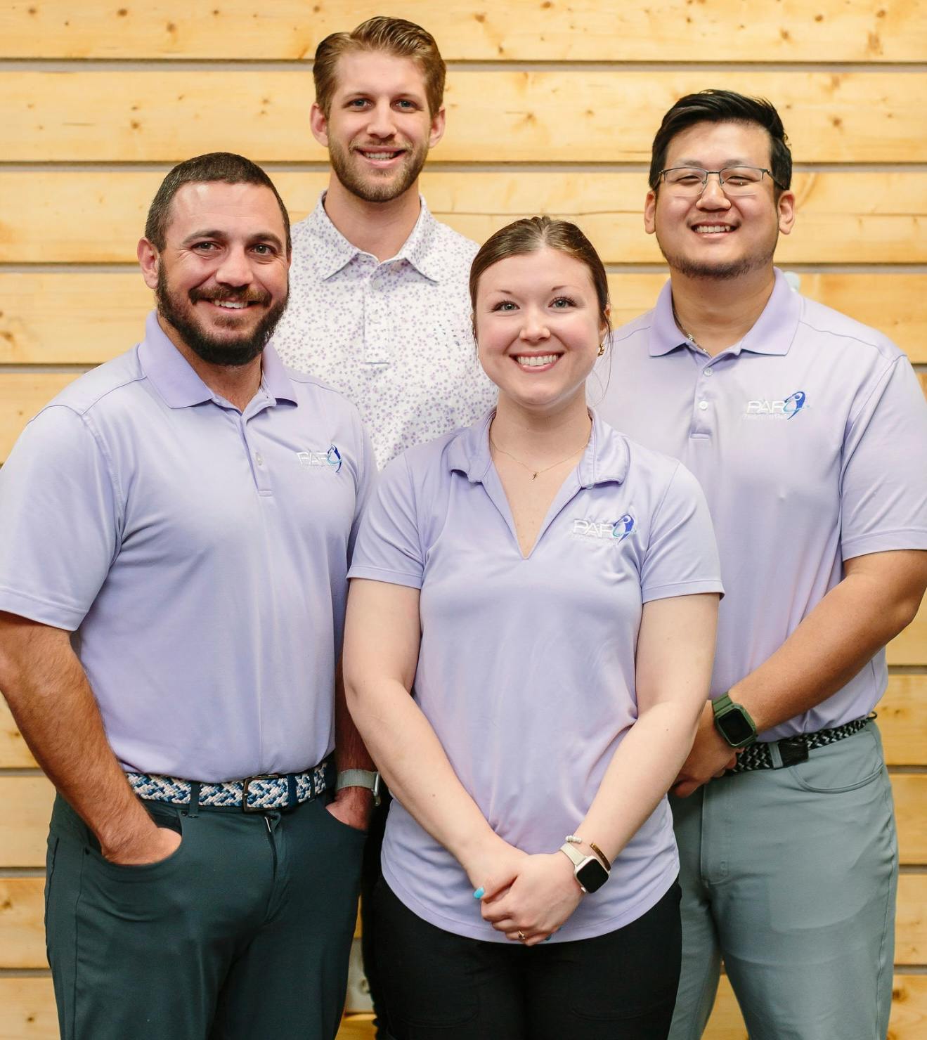 Four members of the PAR Physical Therapy team in matching polo shirts, smiling in front of a wood-slat wall