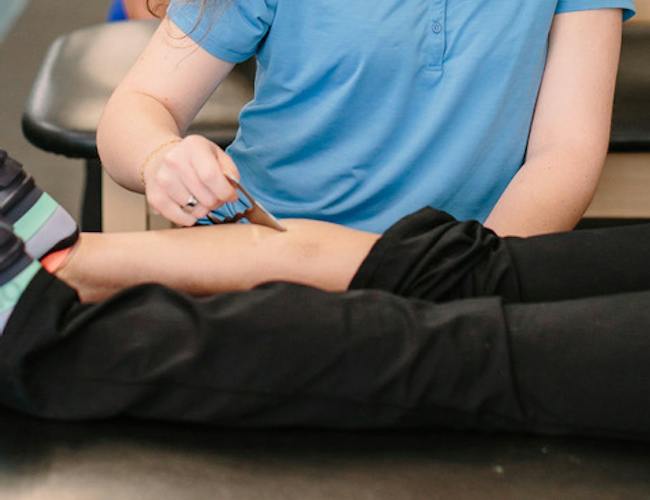 A physical therapist using a hand-held instrument for soft tissue scraping