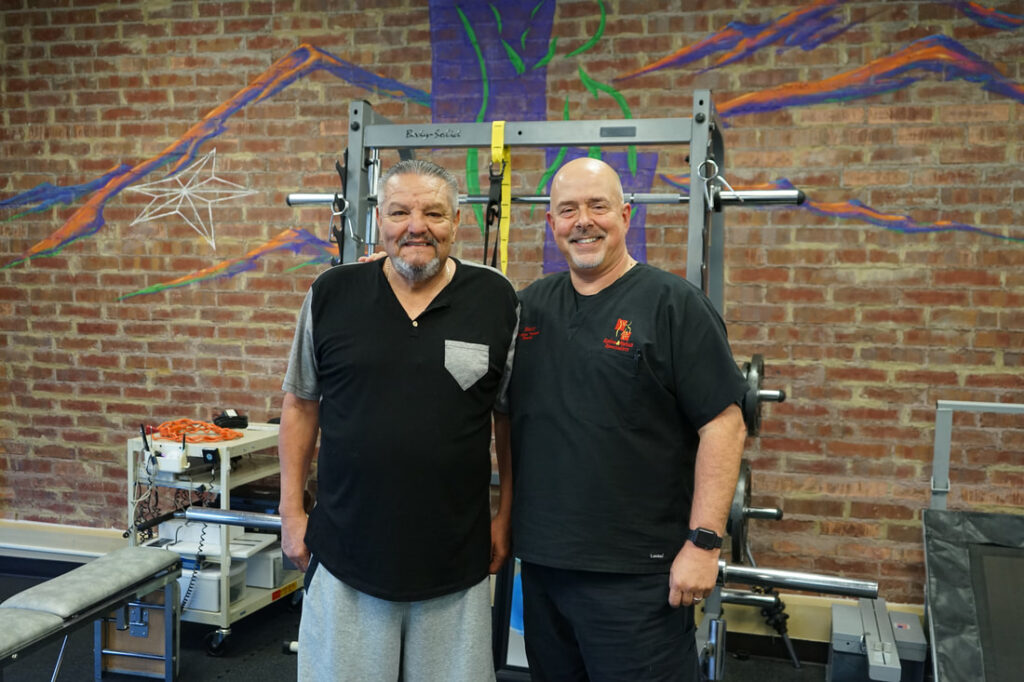 Two men, a patient and a therapist, standing together in the clinic gym