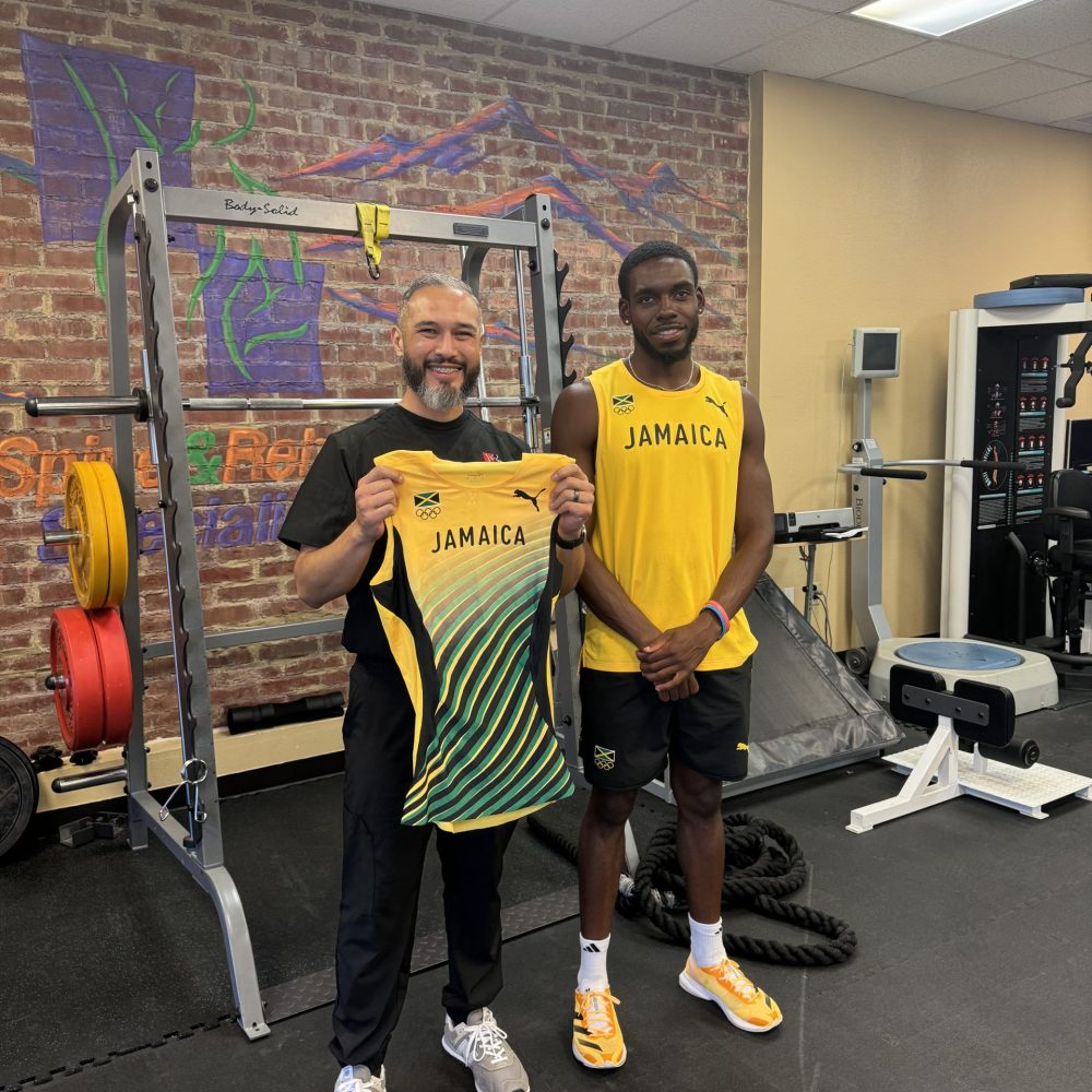 Two men holding up a Jamaica jersey in the gym