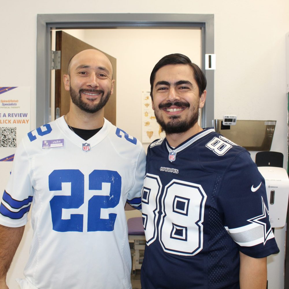 Two Spine & Rehab Specialists team members smiling in football jerseys in the clinic hallway