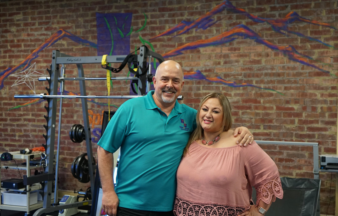 A patient and a Spine & Rehab Specialists therapist smiling together in the clinic gym, holding a framed certificate