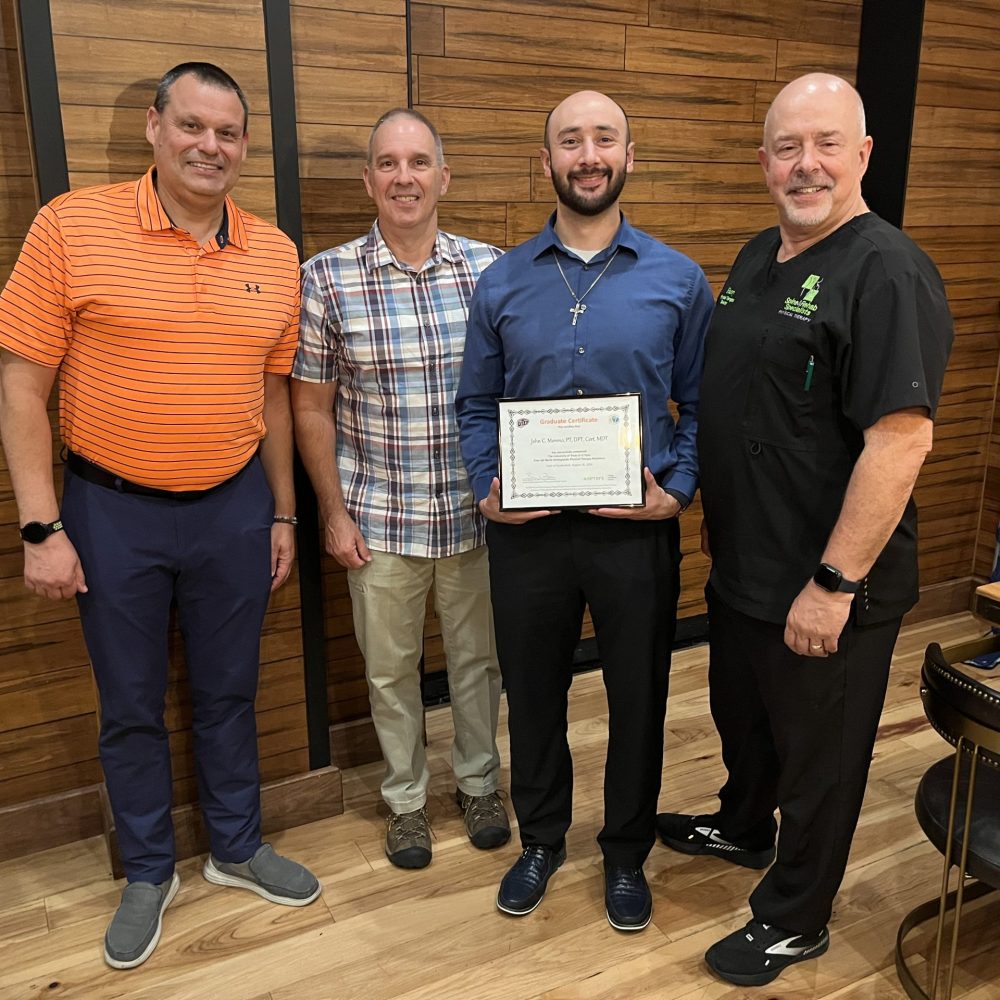 Four members of the Spine & Rehab Specialists team standing together with a framed certificate
