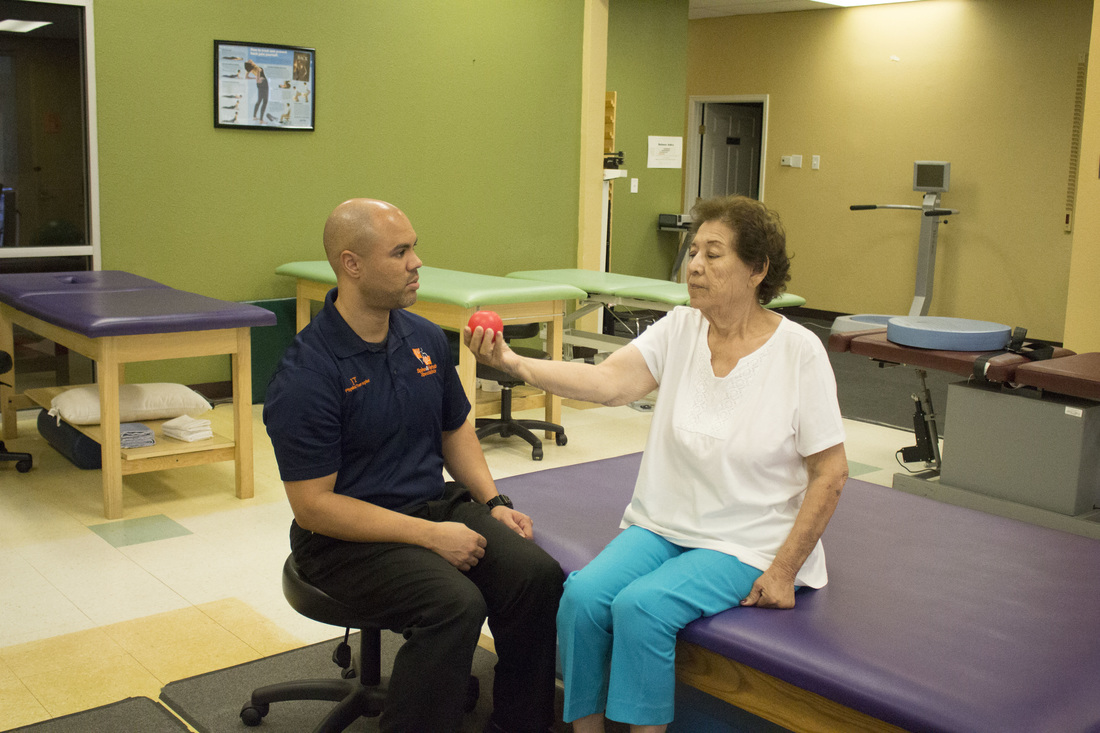 An older patient doing an exercise with a ball under a therapist's guidance